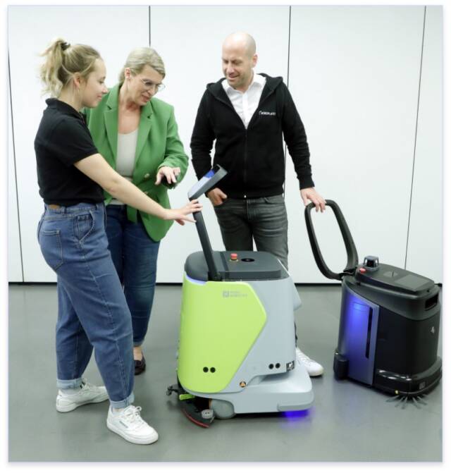 RoboPlanet Mitarbeiterin Evelyn Zühl und RoboPlanet Head of Sales Alexander Kiss mit Kundin am Touchscreen des Pudu CC1