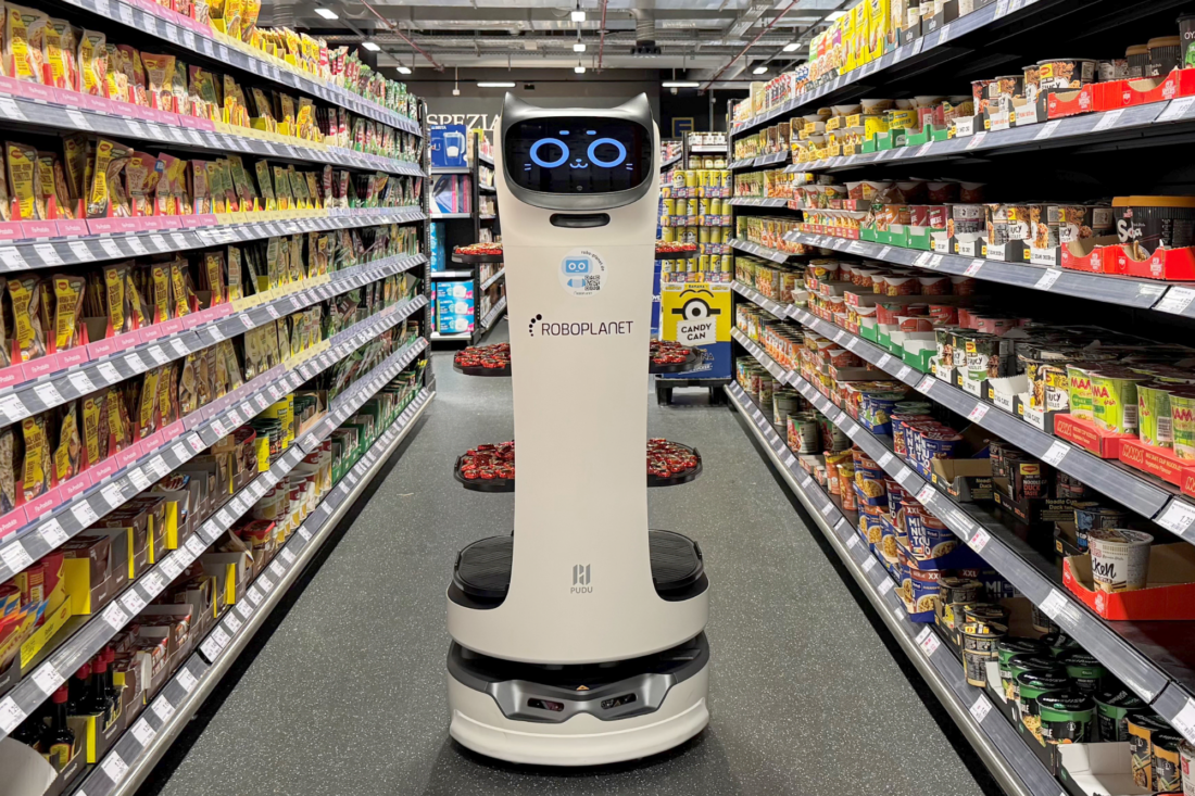 Pudu BellaBot von RoboPlanet mit Häppchen auf den Ablagen fährt durch Regalreihen im Edeka