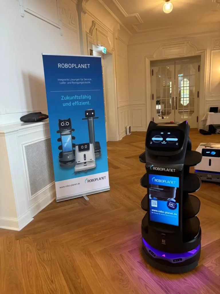 Pudu BellaBot Pro von RoboPlanet auf einer Veranstaltung mit Roll-up von RoboPlanet im Hintergrund als Hochkantbild